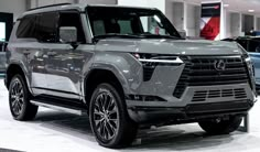 a silver suv is on display in a showroom with other cars behind it and people standing around