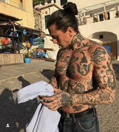 a man with tattoos on his chest and arm is holding a shirt in the street