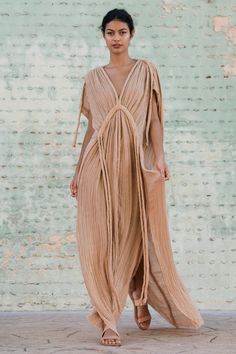 a woman standing in front of a brick wall wearing a dress with fringes on it