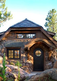 a stone house with a black door and windows on the outside, surrounded by rocks