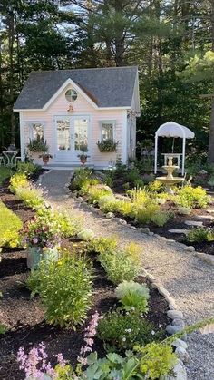 a white house surrounded by lots of trees and flowers in front of the house is a gravel path that leads to an outdoor seating area