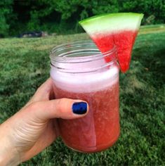 a person holding a glass with a drink in it and a slice of watermelon on top