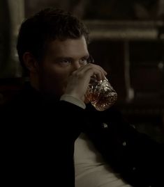 a man sitting down drinking from a glass in front of his face and looking off to the side