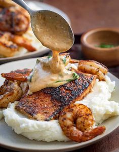 a plate with shrimp, mashed potatoes and sauce being drizzled over