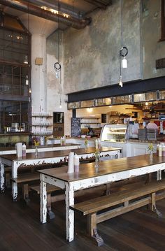 an empty restaurant with wooden tables and benches in front of the counter, along with hanging lights