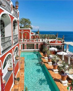 an outdoor swimming pool surrounded by potted plants next to the ocean in front of a red and white building