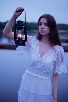 a woman holding a lantern in front of her face and wearing a white dress with ruffles