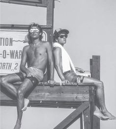 two men sitting on a wooden bench in front of a sign