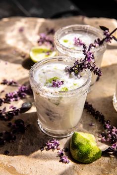 two glasses filled with ice and lavender sprinkled on top of a stone slab