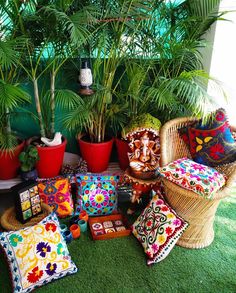 a collection of colorful cushions and pillows on the ground in front of a potted plant