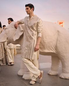 a man standing next to an elephant statue in front of other people wearing white outfits