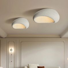 two lights that are on the ceiling above a couch in a room with white walls