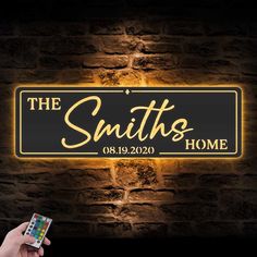 the smiths home illuminated sign in front of a brick wall with a hand holding a remote control