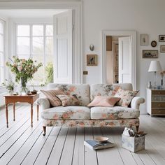 patterns mix perfectly in this white living room: a white paneled floor with white walls and decor  and a two seater upholstered sofa with floral pattern - all come together seamlessly. Floral Sofa Living Room, Patterned Sofa, Chaise Sofa Living Room, Floral Couch, Floral Sofa, Elevated Homes, Printed Sofa, Room Book, Cottage Living Rooms