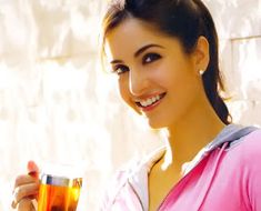 a woman holding a glass of tea and smiling at the camera while standing in front of a wall