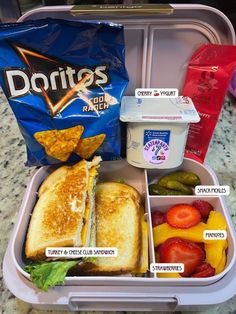 an open lunch box with sandwiches, fruit and yogurt