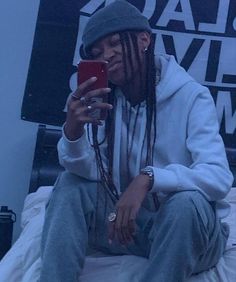 a man with dreadlocks is sitting on a bed and looking at his cell phone