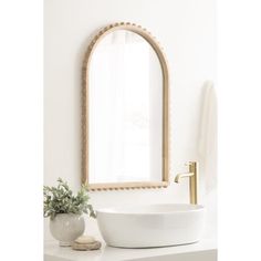 a white sink sitting under a mirror next to a potted plant and a gold faucet