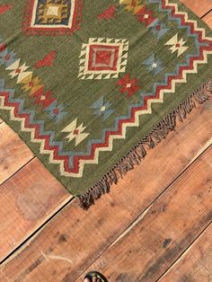 someone is standing on the wooden floor next to a green rug with colorful designs and fringes