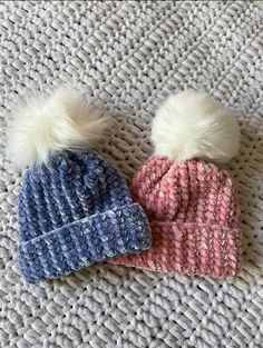 two knitted hats with pom - poms are laying on the floor next to each other