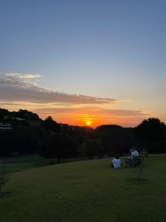 people are sitting in the grass at sunset