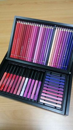 a wooden table topped with two trays filled with different colored crayon pencils