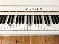 a white piano sitting on top of a wooden floor next to a sign that says a - geyer