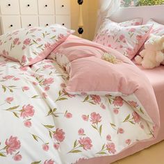 a bed with pink and white flowers on the comforter, pillows and teddy bear