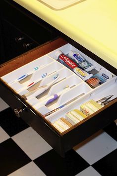 an open drawer with toothbrushes and other items in it on a black and white checkered floor