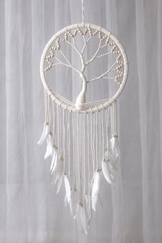 a white dream catcher with feathers hanging from it's sides and a tree on top