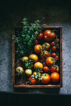 a wooden box filled with lots of different types of tomatoes and greens on top of a table