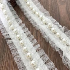 two white garters with pearls and lace on a wooden surface, next to a brush