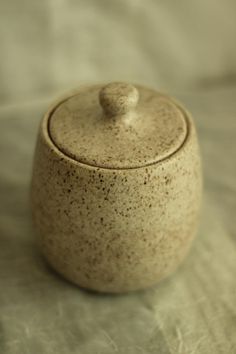 a ceramic container with a wooden lid on a white cloth covered tablecloth, top view