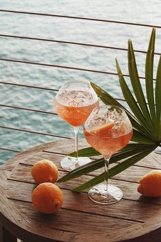 two wine glasses sitting on top of a wooden table next to oranges and palm leaves