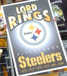 two people holding up a sign that says lord of the rings and pittsburgh footballs