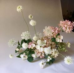 a vase filled with lots of white and pink flowers on top of a table next to a wall