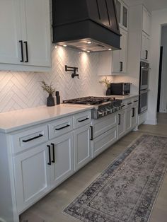 a kitchen with white cabinets and black stove top hood over the range in front of an area rug