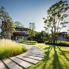 a stone path in front of a house with tall grass and trees on the other side