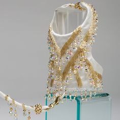 a white and gold beaded dress on display in front of a glass block with an attached necklace