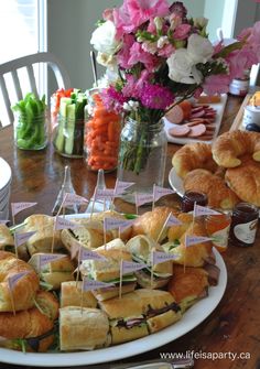 a table topped with sandwiches and croissants on top of white plates next to flowers