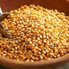 a wooden bowl filled with corn kernels and a metal spoon in it's center