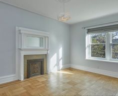 an empty living room with hard wood floors and a fire place in the corner between two windows