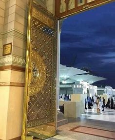 an open door with arabic writing on it and people walking around in the background at night