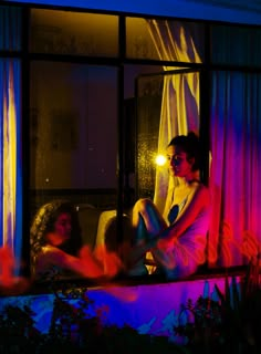 two women sitting on a window sill in the dark