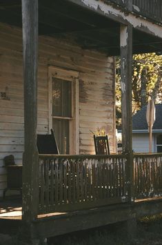 an old wooden porch with rocking chairs on the front and side of it, in front of a white house