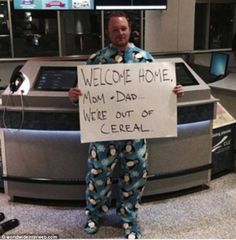 a man in pajamas holding a sign that says welcome home from dad we're out of cereal