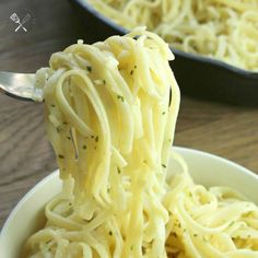 a fork full of spaghetti being held up by someone's hand on a wooden table