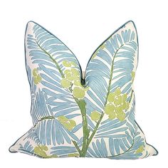 a blue and green pillow with large leaves on the front, sitting on a white surface