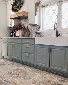 a kitchen with blue cabinets and white counter tops, an area rug and a wreath on the window sill