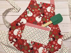 a red apron with white polka dots and snowmen on it next to a green spatula